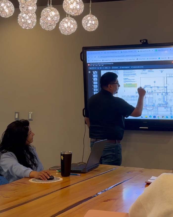 A professional home designer at H Design using a large digital screen to review and explain a detailed residential floor plan during a client consultation in the office studio.